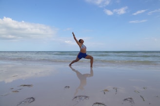 A yoga mat laid out on soft sand beside turquoise water under a clear sky.