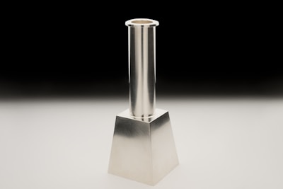 A sleek metal art candlestick glowing softly on a wooden table.