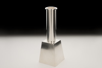 A metallic candlestick with a sleek, modern design featuring a cylindrical shaft and a square base. It is positioned against a black to white gradient background, highlighting its reflective surface.