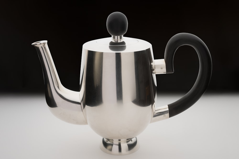 a silver tea pot with a black handle