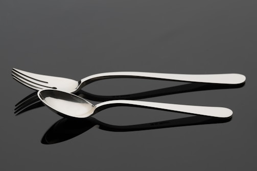 An elegant stainless steel fork and spoon set shining under soft natural light.