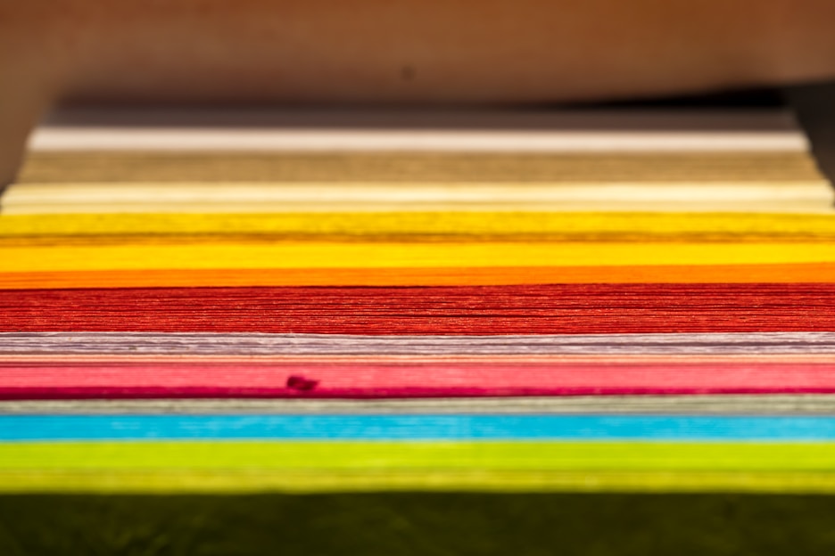 A stack of assorted colorful paper sheets neatly arranged on a wooden desk