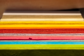 A stack of colored paper arranged horizontally, displaying a wide range of vibrant hues. The sheets are neatly aligned, showcasing visible layers and texture.