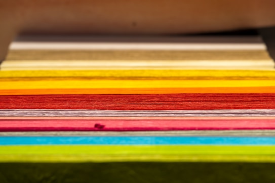 A stack of colored paper arranged horizontally, displaying a wide range of vibrant hues. The sheets are neatly aligned, showcasing visible layers and texture.