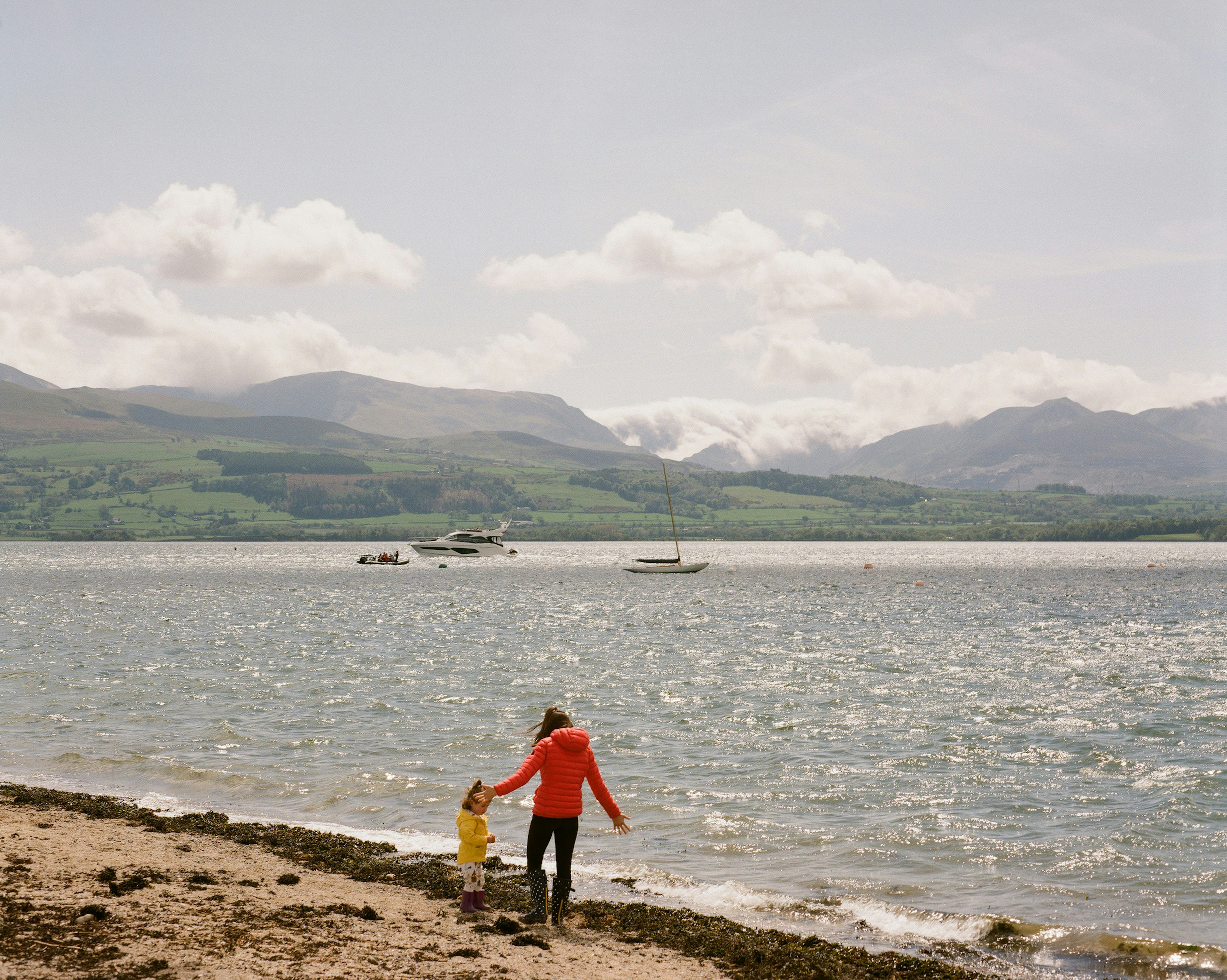 a woman and a child are standing on the shore of a lake