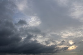 Dark and dense clouds cover the sky, with some lighter patches allowing glimpses of sunlight. The overall sky is mostly overcast, suggesting an impending storm or rain.