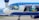 A Brussels Airlines airplane is parked at an airport, featuring animated Smurf characters on its exterior. One Smurf is dressed as a pilot, holding the controls in the cockpit, while another is dressed as a chef inside the plane.