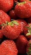 Fresh, ripe strawberries with vibrant red color and tiny seeds covering their surface. Green leaves are visible at the top of some strawberries, adding contrast.