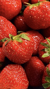 Fresh, ripe strawberries with vibrant red color and tiny seeds covering their surface. Green leaves are visible at the top of some strawberries, adding contrast.