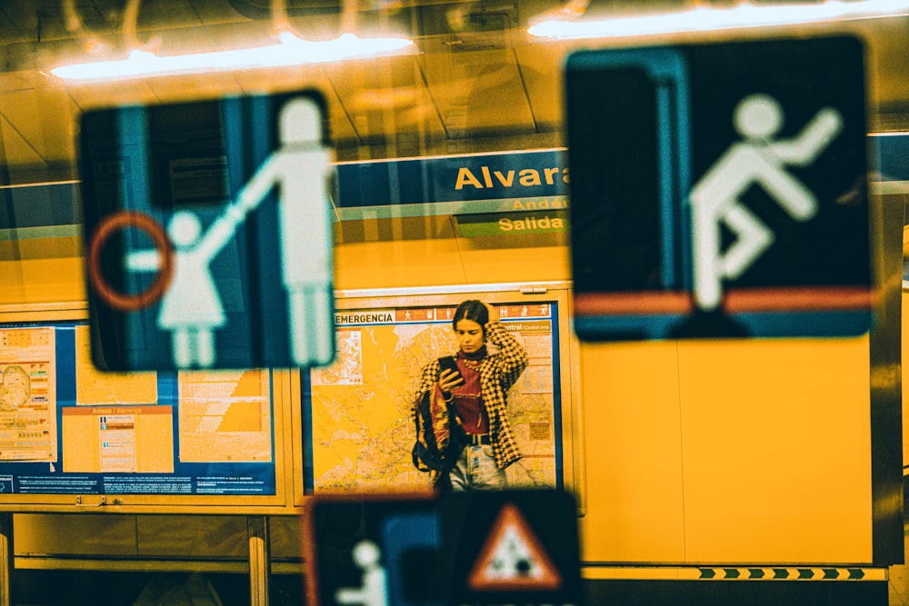 a woman standing in a train station next to a sign