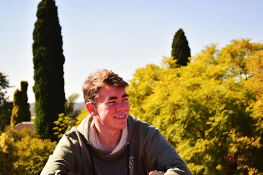 A young adult smiling while journaling outdoors, surrounded by nature and sunlight.