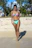 A joyful woman wearing a vibrant bikini standing on a sandy beach with palm trees in the background.