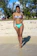 A joyful woman wearing a vibrant bikini standing on a sandy beach with palm trees in the background.