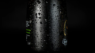 Close-up of a crystal-clear water drop sliding down a glass bottle labeled Aquaviva.