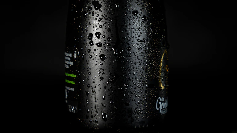 Close-up of a matte black Senna bottle glowing under neon yellow light with water droplets.