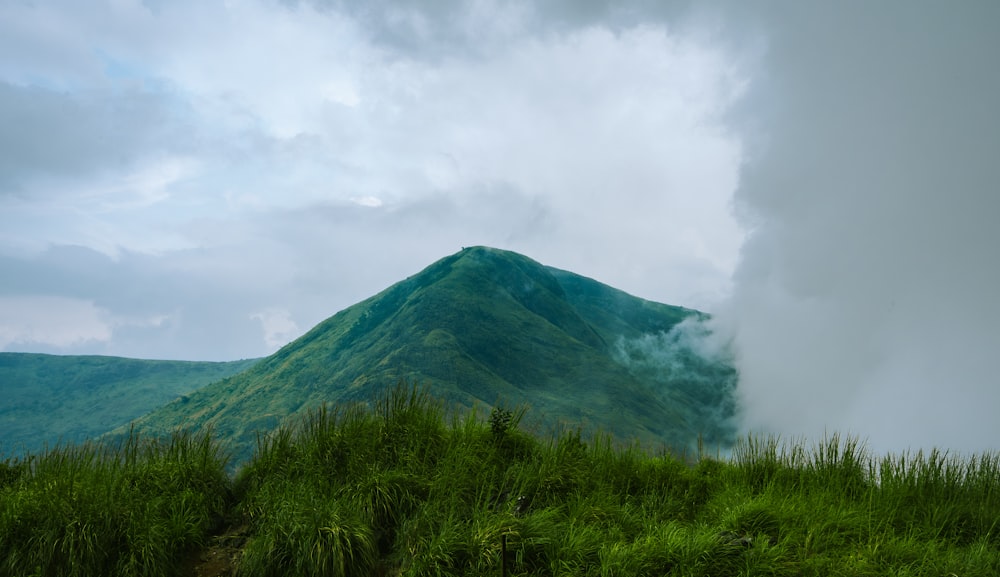 a large green mountain with a cloud in the sky