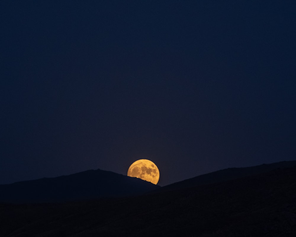 a full moon rising over a mountain range