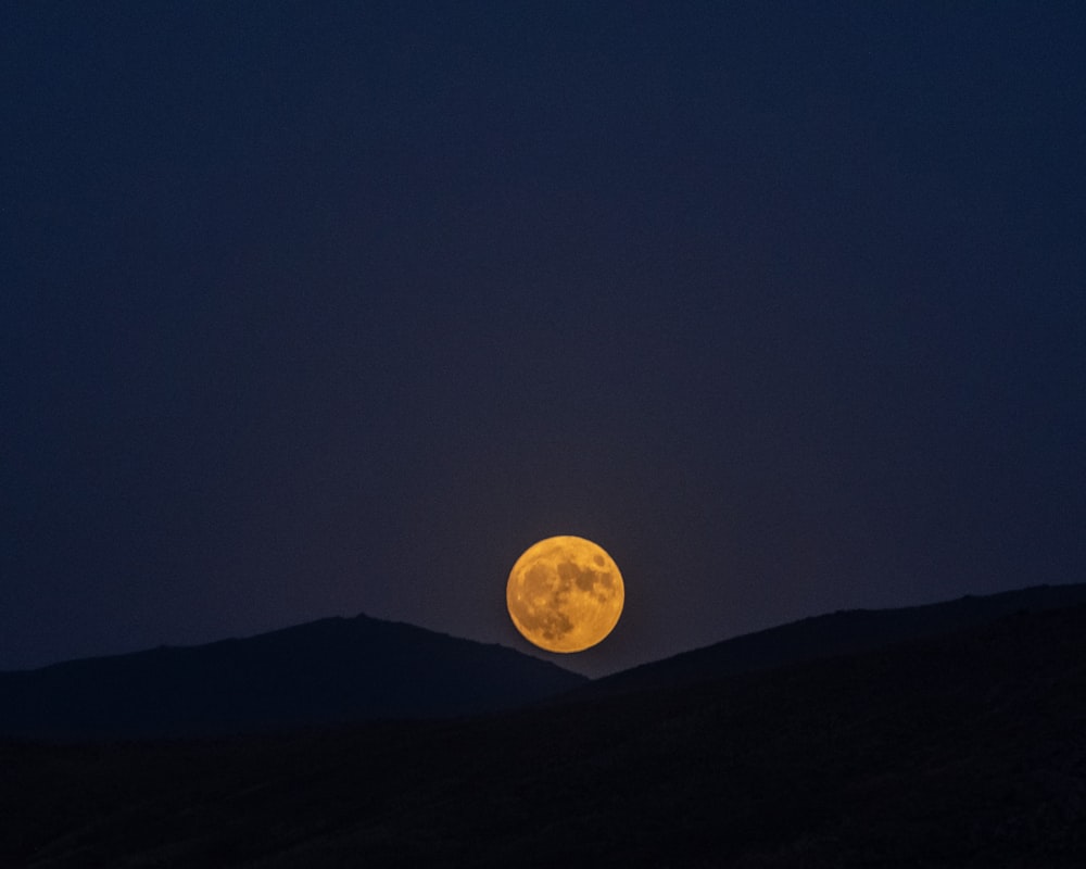 a full moon is seen in the sky above a hill