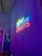 A vibrant neon sign with the text 'Follow Your F*cking Dreams' is mounted on a textured gray wall. The sign's colors include bright yellow, blue, and pink, casting a colorful glow. A decorated area with a surfboard, a beaded curtain, and a fire extinguisher sign is visible on the left.