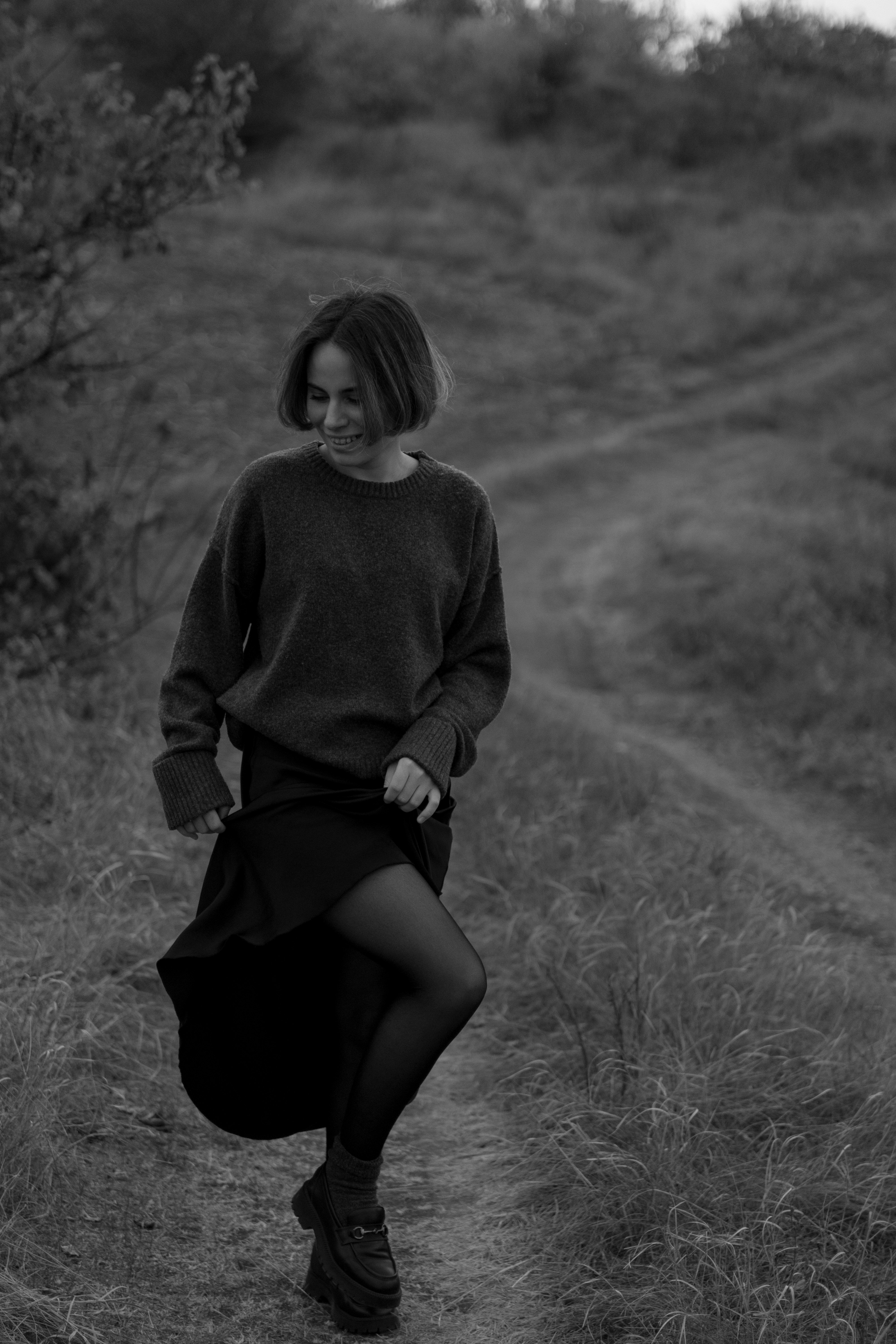 a woman walking down a dirt road in a black and white photo
