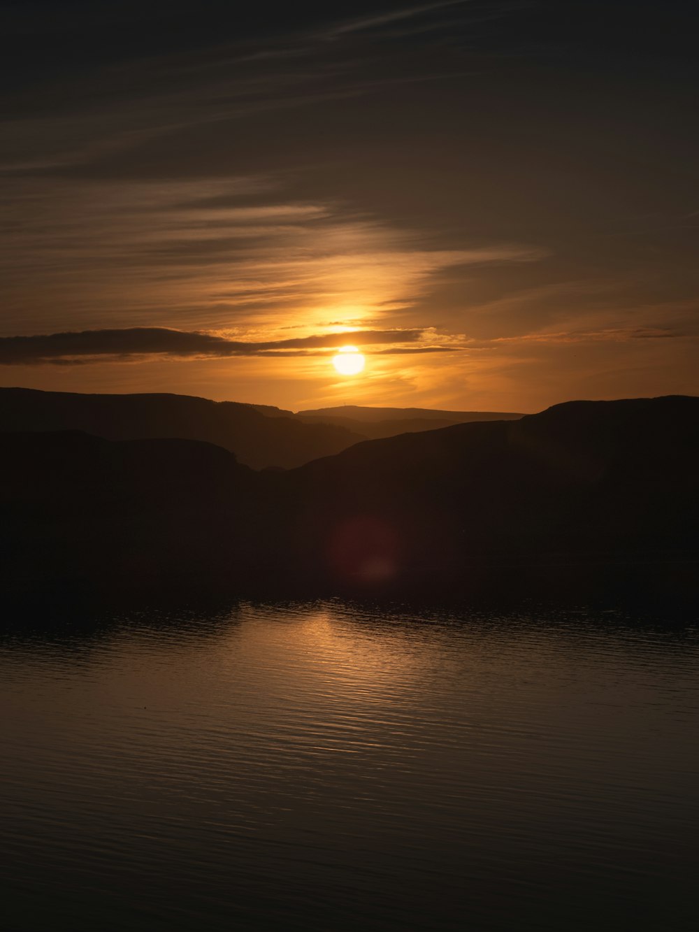 the sun is setting over a lake with mountains in the background