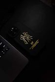A sleek minimalist phone case in matte black with subtle gold accents placed on a wooden desk beside a notebook.