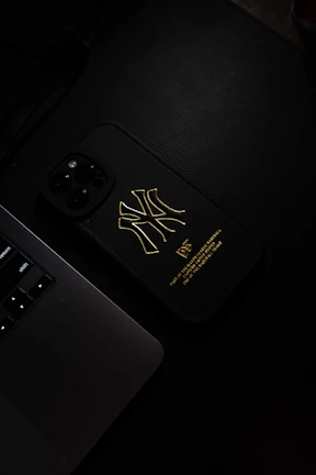 A sleek minimalist phone case in matte black with subtle gold accents placed on a wooden desk beside a notebook.