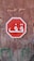A red stop sign with white Arabic text is mounted on a weathered wooden wall. The wall shows signs of age with peeling paint and visible texture. Above the sign, there is some faded lettering on the wood.