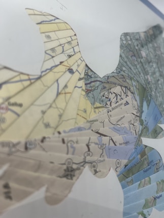 A map collage in the shape of a stylized bird, featuring various geographic elements like rivers, roads, and locations. The map is intricately cut and layered to form the bird shape, showcasing a mix of topographic and roadmap patterns with different colors.