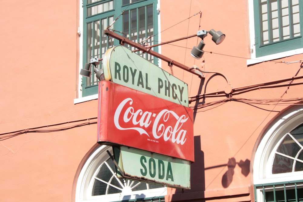 a neon coca cola sign hanging from the side of a building