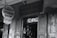 A black-and-white photograph of a storefront with a sign reading 'Rev. Zombie's Voodoo Shop' offering readings and rituals. The entrance has weathered wooden doors and a slightly eerie appearance, with various flyers and signs posted nearby.