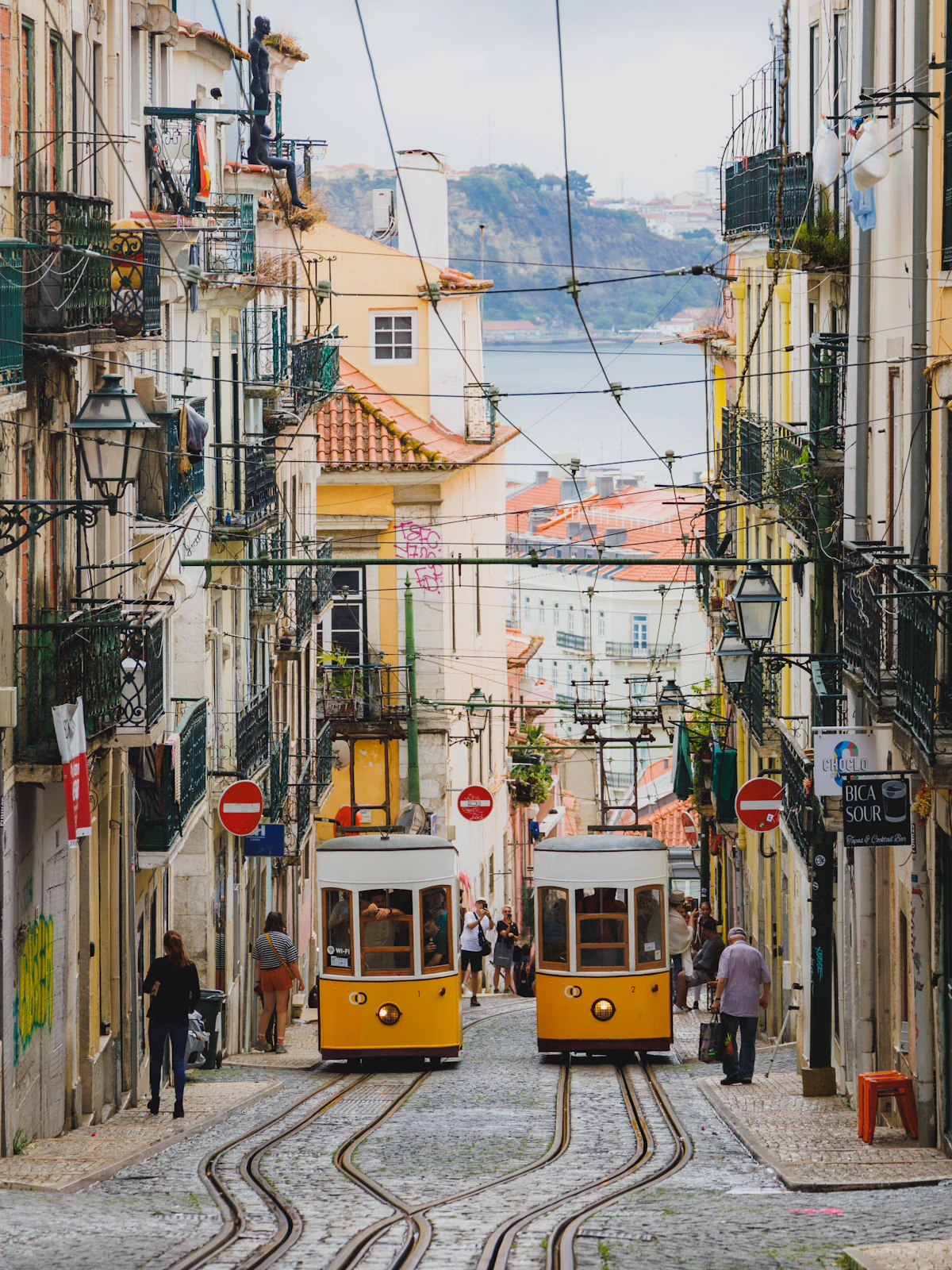 A narrow Lisbon street lined with tiled buildings and overhead tram wires