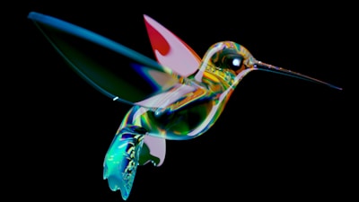 A vibrantly colored abstract depiction of a hummingbird with a glass-like texture and prismatic effect. The bird is set against a stark black background, highlighting its iridescent colors and elongated beak.
