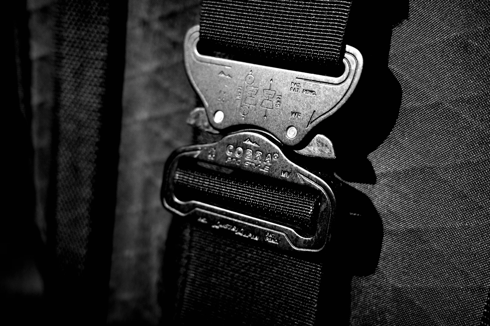 Macro detail of a metal quick-release buckle and thick nylon webbing straps against rugged technical Cordura bag fabric