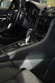 The interior of a luxury car featuring a sleek black steering wheel, a gearshift, and a modern dashboard with a digital display. The seats and console are upholstered in dark leather, with detailed stitching visible.