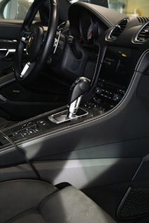 The interior of a luxury car featuring a sleek black steering wheel, a gearshift, and a modern dashboard with a digital display. The seats and console are upholstered in dark leather, with detailed stitching visible.