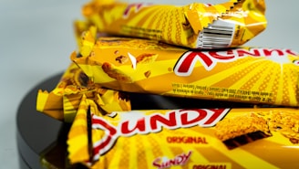 Several yellow-wrapped chocolate bars with a distinctive red logo and images of waffle texture on the packaging are stacked together on a reflective black surface.