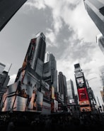 Skyscrapers rise against a cloudy sky, adorned with bright, large advertisements and digital billboards. The urban environment is dynamic, with various colorful ads promoting different brands and shows.