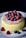 A fluffy, golden-brown cake topped with a dusting of powdered sugar, garnished with fresh raspberries and blueberries. The cake is placed on a white plate against a dark background, highlighting its texture and vibrant colors of the fruits.