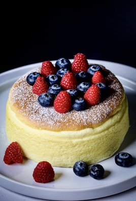 A colorful gluten-free cake topped with fresh berries on a rustic wooden table.