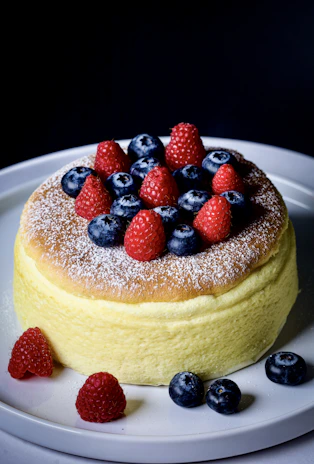 A close-up of a freshly baked, golden-brown cake topped with vibrant fresh berries and a light dusting of powdered sugar.