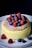 A fluffy, golden-brown cake topped with a dusting of powdered sugar, garnished with fresh raspberries and blueberries. The cake is placed on a white plate against a dark background, highlighting its texture and vibrant colors of the fruits.