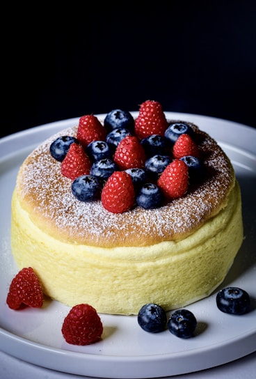 A vibrant mixed berry cake topped with blueberries, raspberries, and a dusting of powdered sugar.