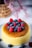 A fluffy, golden-brown cheesecake is topped with vibrant blueberries and raspberries. The cake sits elegantly on a white plate, with additional berries scattered around. In the background, a decorative woven basket and soft focus pink flowers add a touch of warmth and elegance.