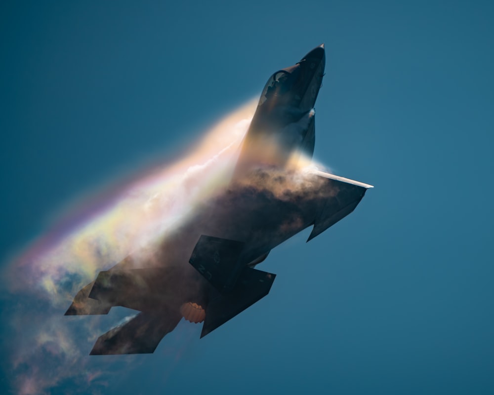 a jet flying through the sky with a rainbow coming out of it