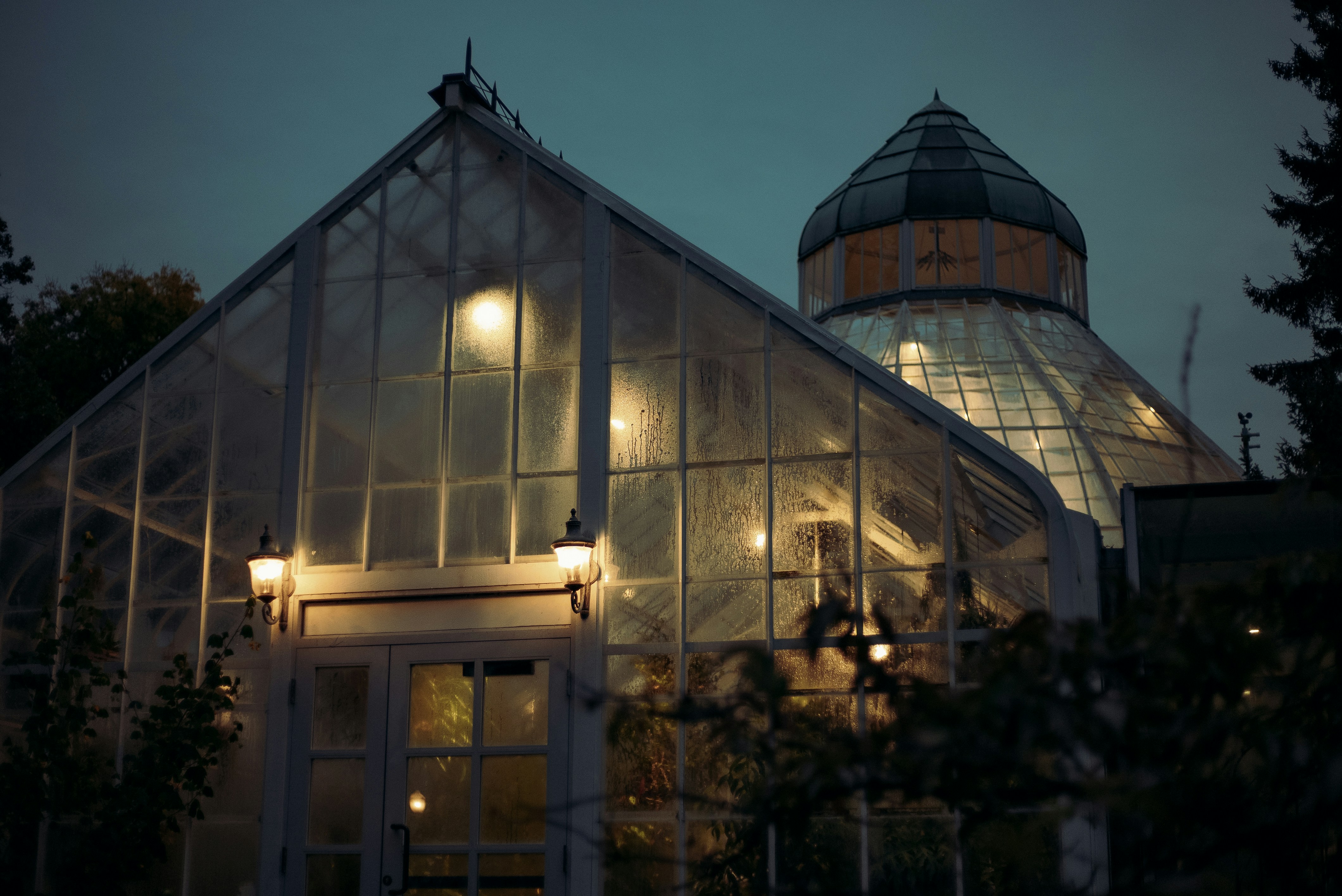 a large glass house with lights inside of it
