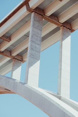 Concrete bridge beams and support columns against a clear blue sky, showcasing structural design and engineering.