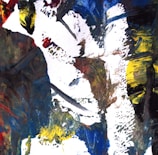 An abstract painting featuring bold, expressive brushstrokes in a mix of colors including blue, yellow, red, black, and white. The composition is dynamic and textured, creating a sense of movement and intensity.