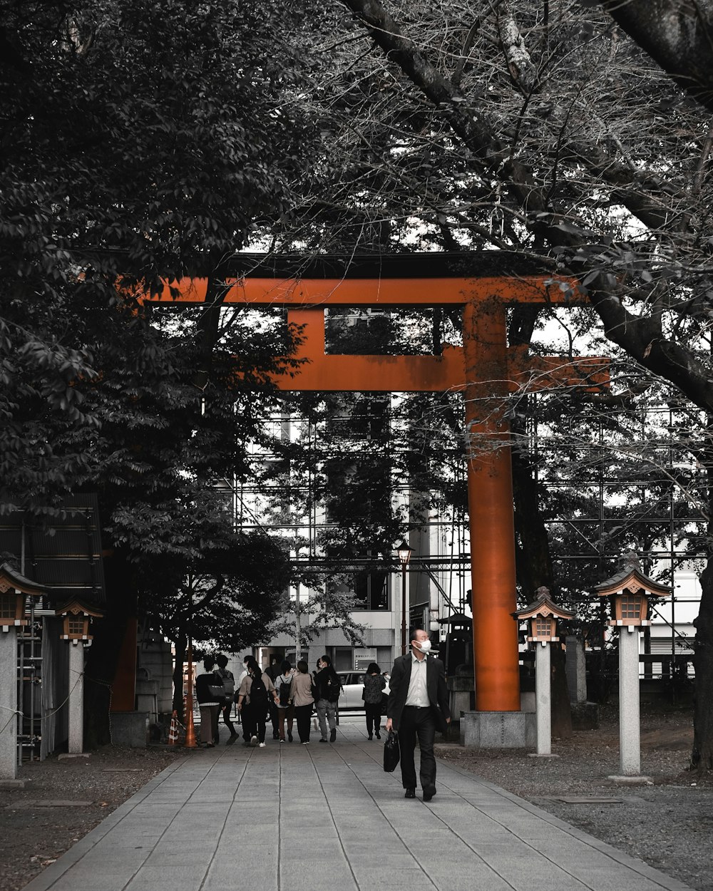 a man walking down a sidewalk under a tall orange tori tori