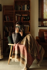 Person listening to audiobook with headphones in a cozy setting.